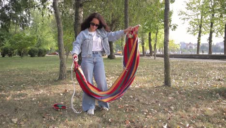 woman setting up a colorful striped hammock in a park
