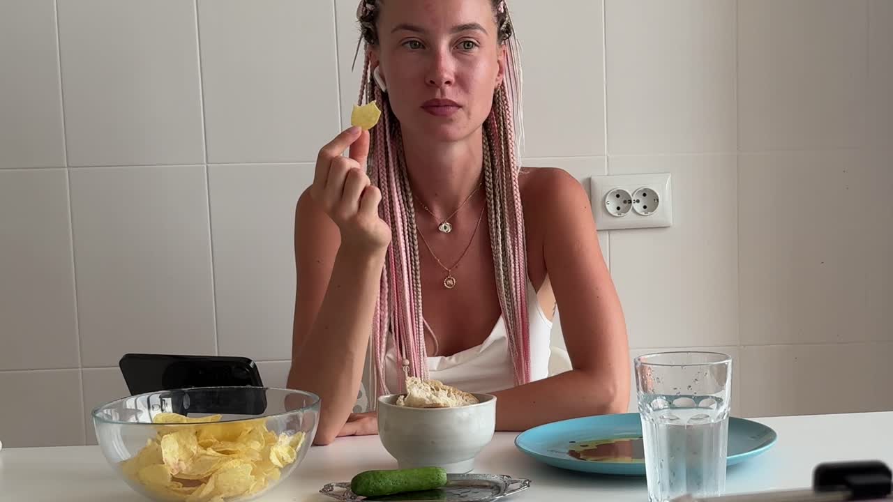 Junge Frau isst Kartoffelchips in einer Küche.