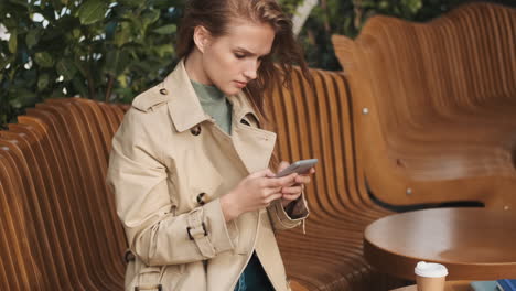 caucasian female student using smartphone in outdoor cafe.