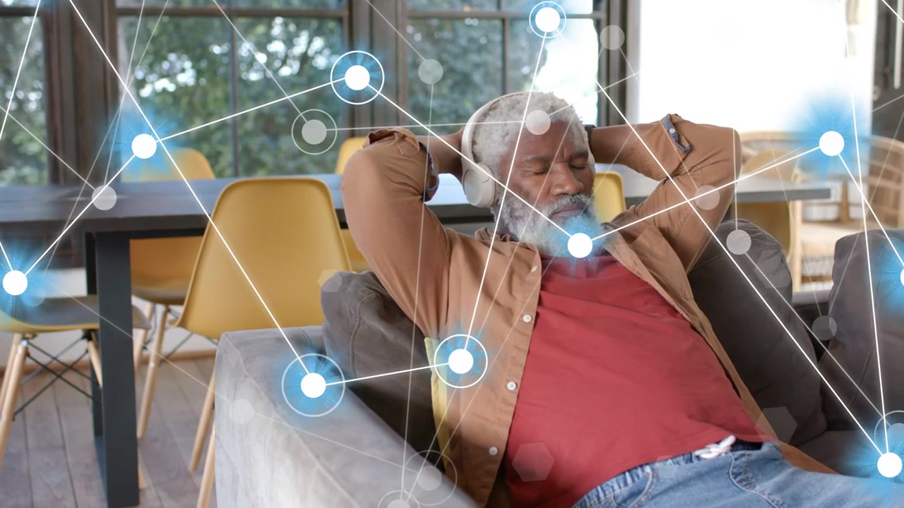 Uomo anziano che si rilassa su un divano grigio, cuffie che emettono suono, nodi di rete tecnologici che crescono intorno a lui.