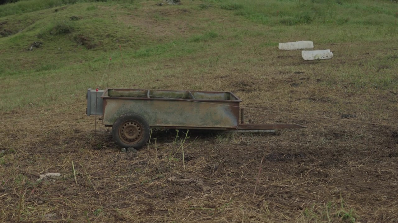 An old rusty farm trailer stands on trampled grass in a hillside pasture on Sao Miguel island in the Azores.