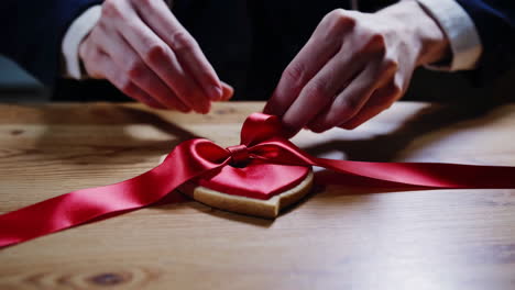 tying a red ribbon bow on a heart-shaped cookie