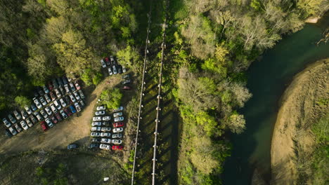 a junkyard with rows of cars by a river in fayetteville, ar during the day, aerial view