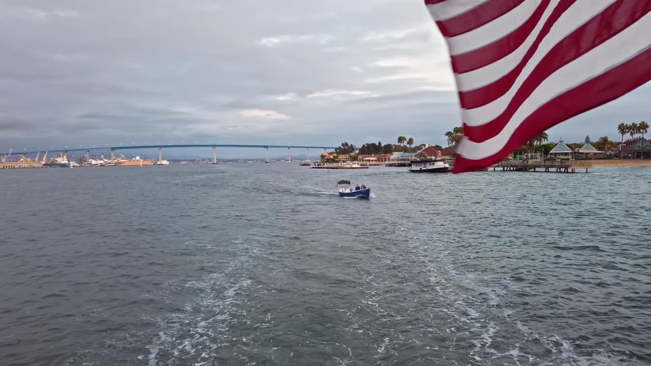 Boat floating on San Diego bay near Coronado bridge. Cloudy sky. USA flag blowing in a wind at the corner. Slow motion