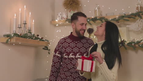 Glückliche-Frau,-Die-Eine-Weihnachtsgeschenkbox-Hält-Und-Ihren-Freund-Zu-Hause-Küsst