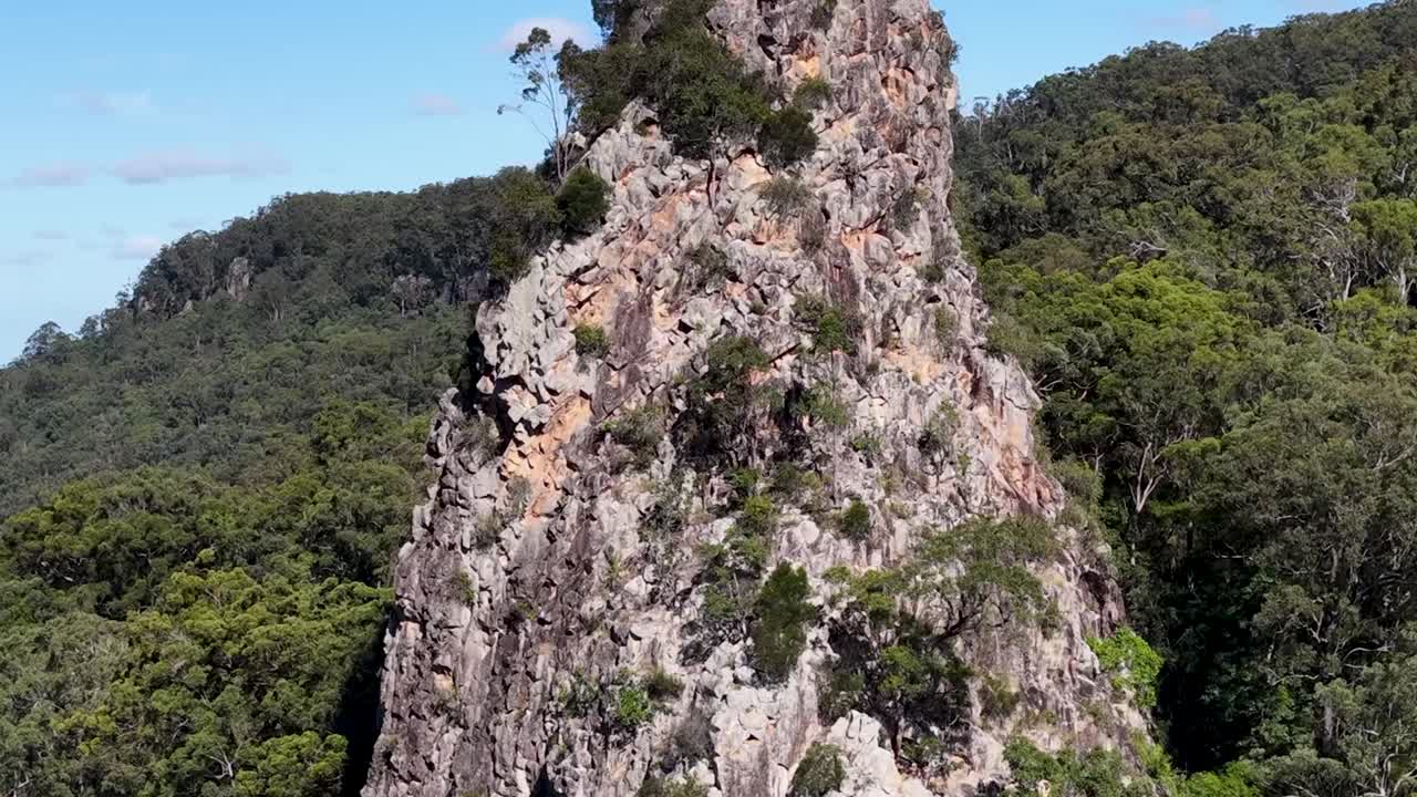 Una ripresa dettagliata con drone si concentra su un'imponente guglia di roccia vulcanica circondata da una fitta foresta