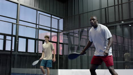 Diverse men playing padel tennis on indoor court, focusing on intense match