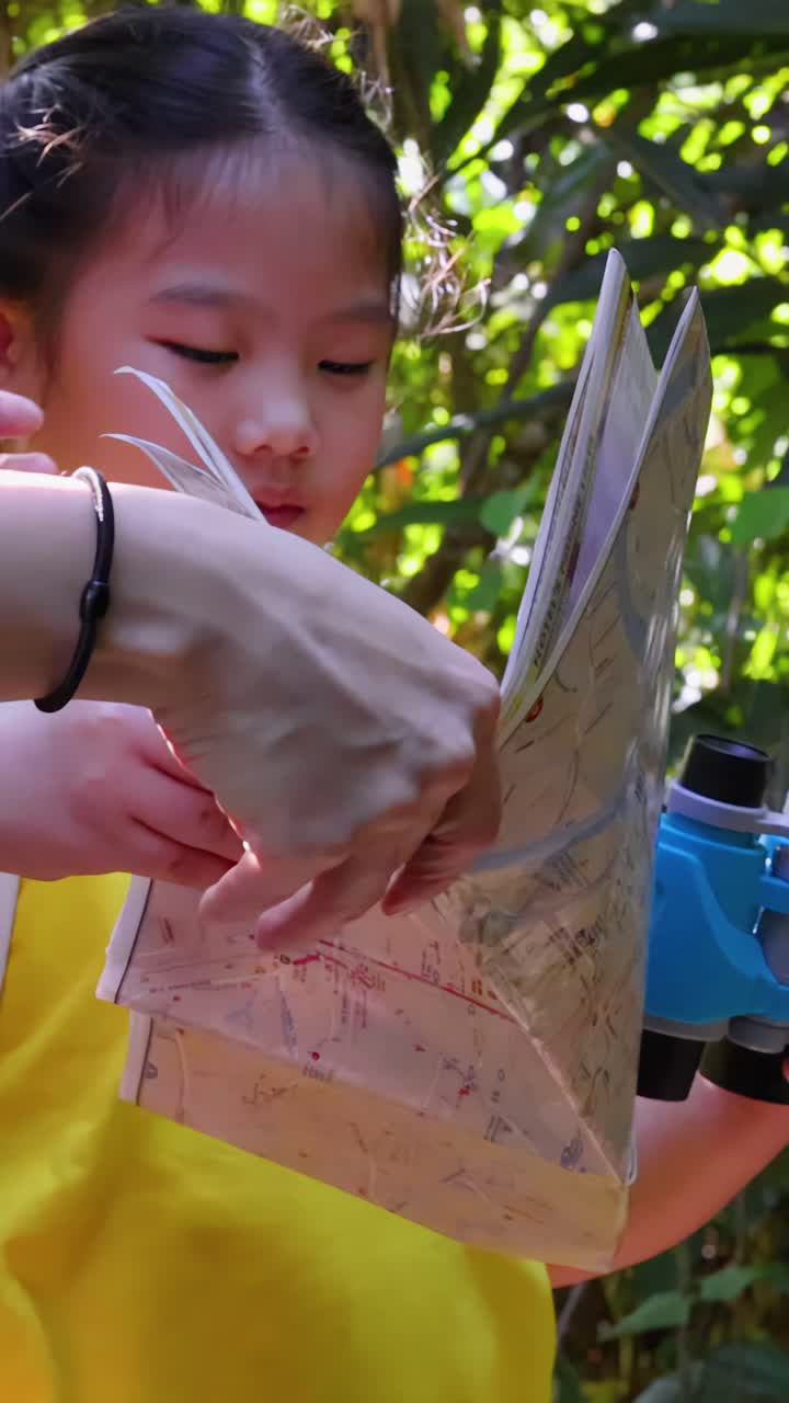 A young girl in a yellow shirt examines a paper map with her mother outdoors