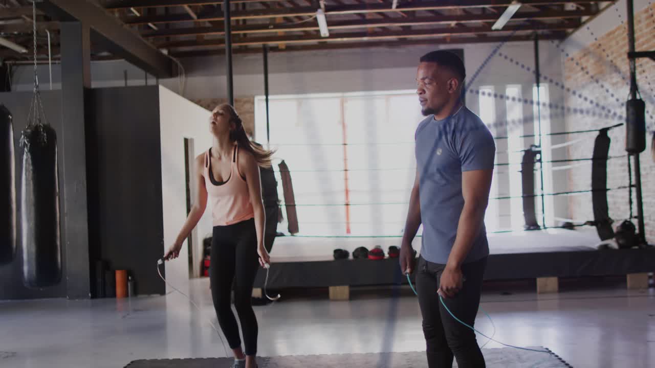 Man and woman jumping rope on gym mat, initiating swing together for cardio training, slowing down