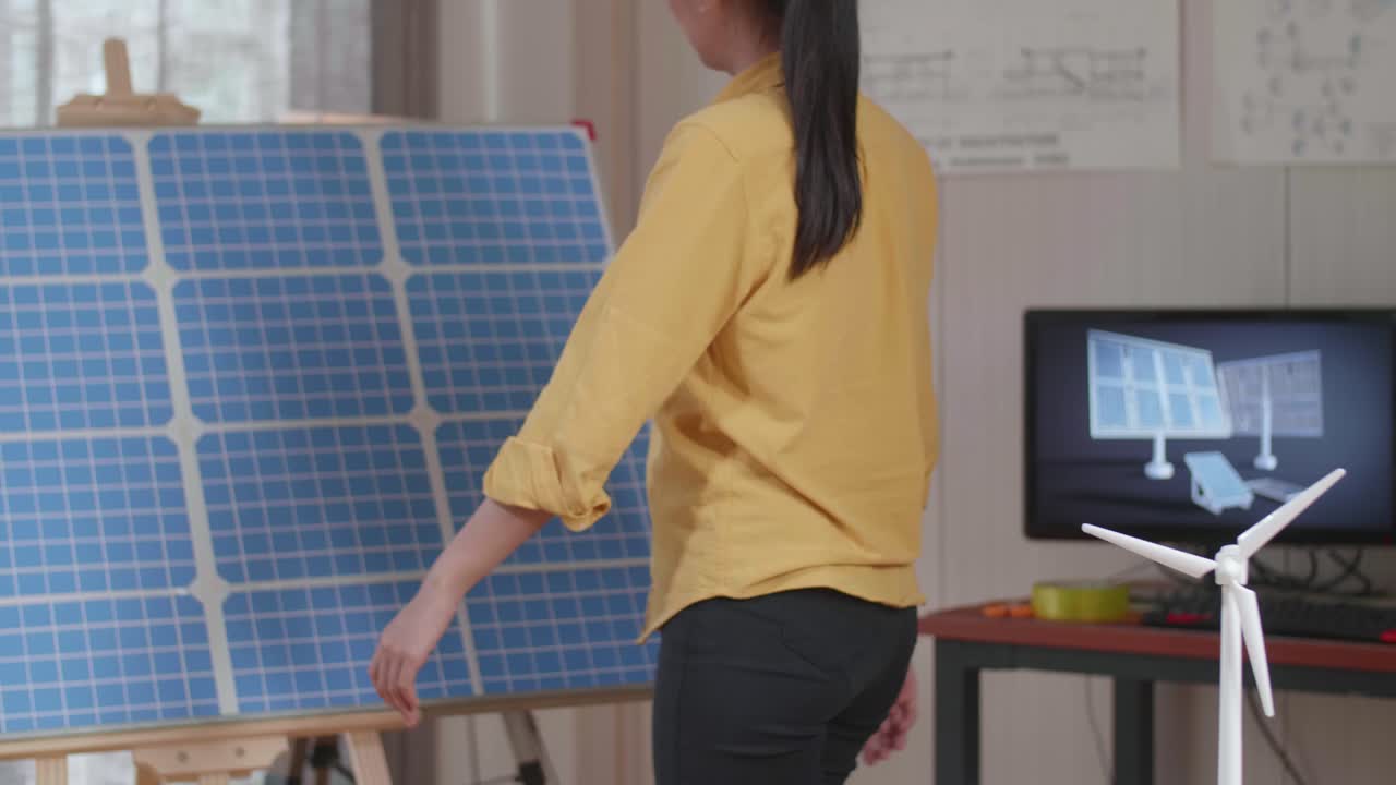 modelo de una pequeña casa con panel solar está en la mesa mientras una mujer entra en la oficina para mirar la célula solar