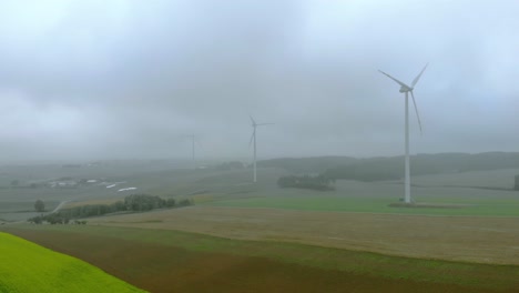 Aerial-footage-close-up-to-wind-farm,-windmill-during-fog,-grey-landscape-around,-renewable-energy-in-the-open-field,-below-natural-landscape,-green-energy-is-important