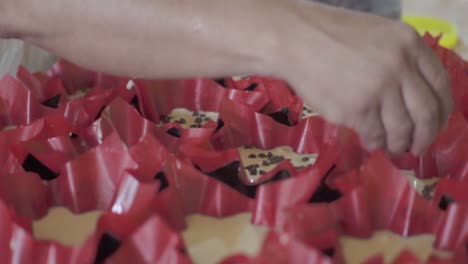 a pastry chef sprinkles chocolate chips into unbaked pastries placed in liners, preparing them for baking.