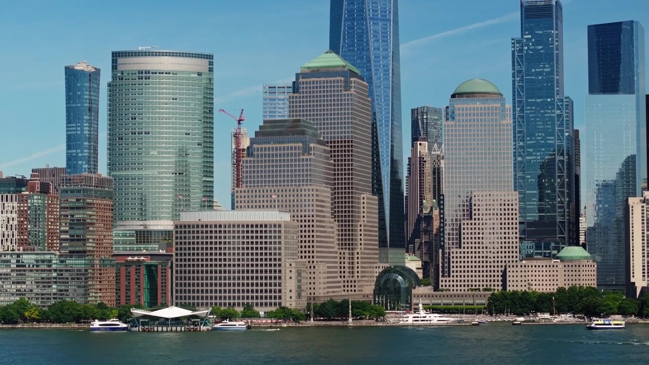 Drone ascende da água do rio Hudson ao longo de edifícios cintilantes de tons cinza, marrom e azul refletindo o céu, NYC
