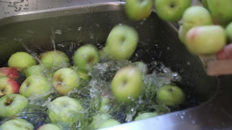 woman pouring green apples on kitchen sink filled with water - handheld, close up