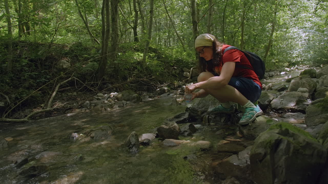 Woman filling water bottle from stream in forest
