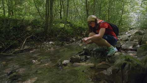 woman filling water bottle from stream in forest