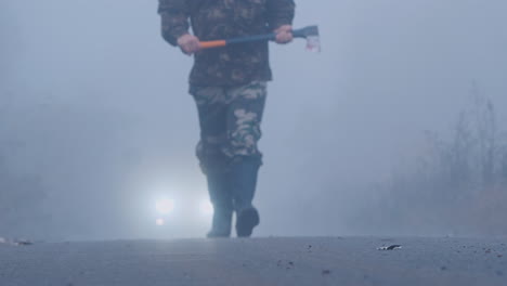 拿着斧头的激进男人在雾中走向汽车