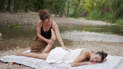 Masseuse-Reibt-Die-Füße-Einer-Frau,-Die-In-Der-Nähe-Des-Plätschernden-Wassers-Eines-Teichs-Liegt