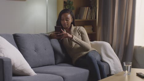 young woman relaxing at home sitting on sofa scrolling through mobile phone 1