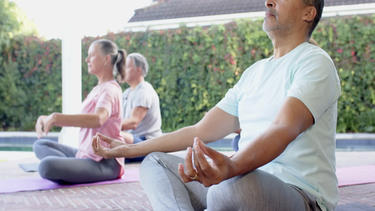 Meditating outdoors, senior friends practicing yoga on mats by pool