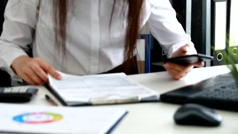 businesswoman using smartphone and filling documents in modern office