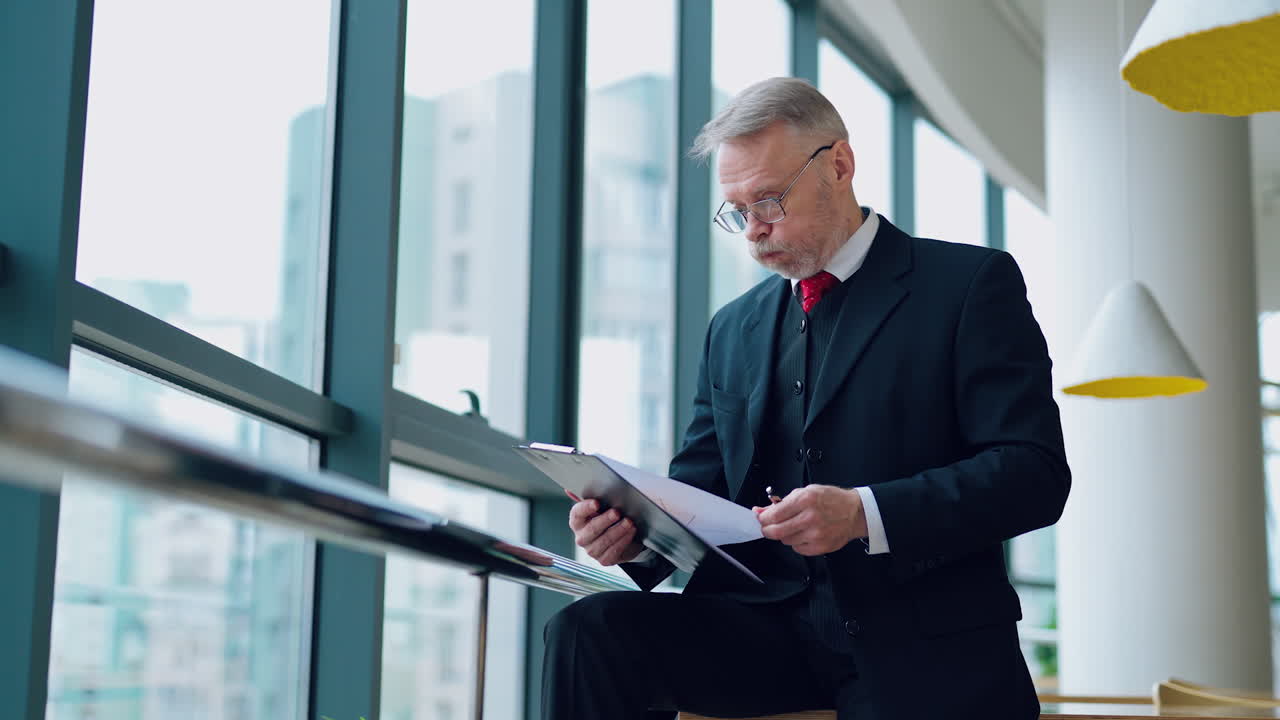 Businessman is working with documents in the office throwing away papers. Video with a senior man near window.