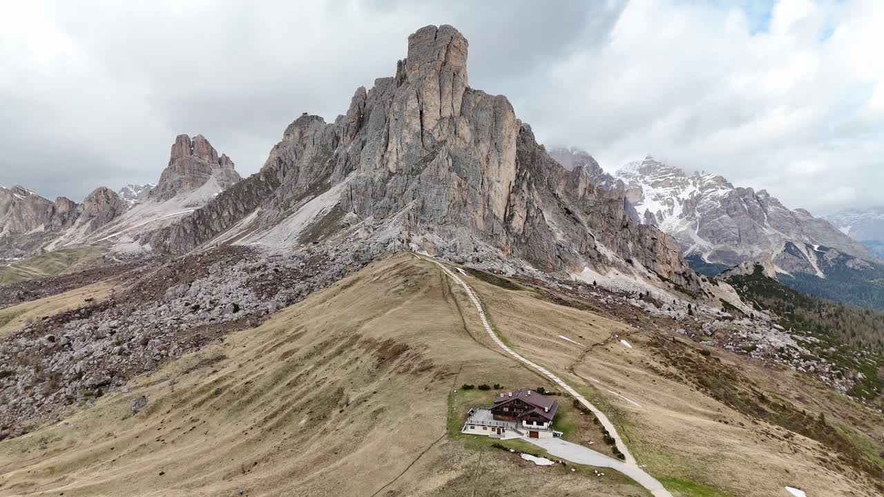 Drone flight over Passo Giau turning from Ra Gusela toward a group of dramatic Dolomite peaks with steep rocky walls. Majestic alpine landscape under soft overcast light