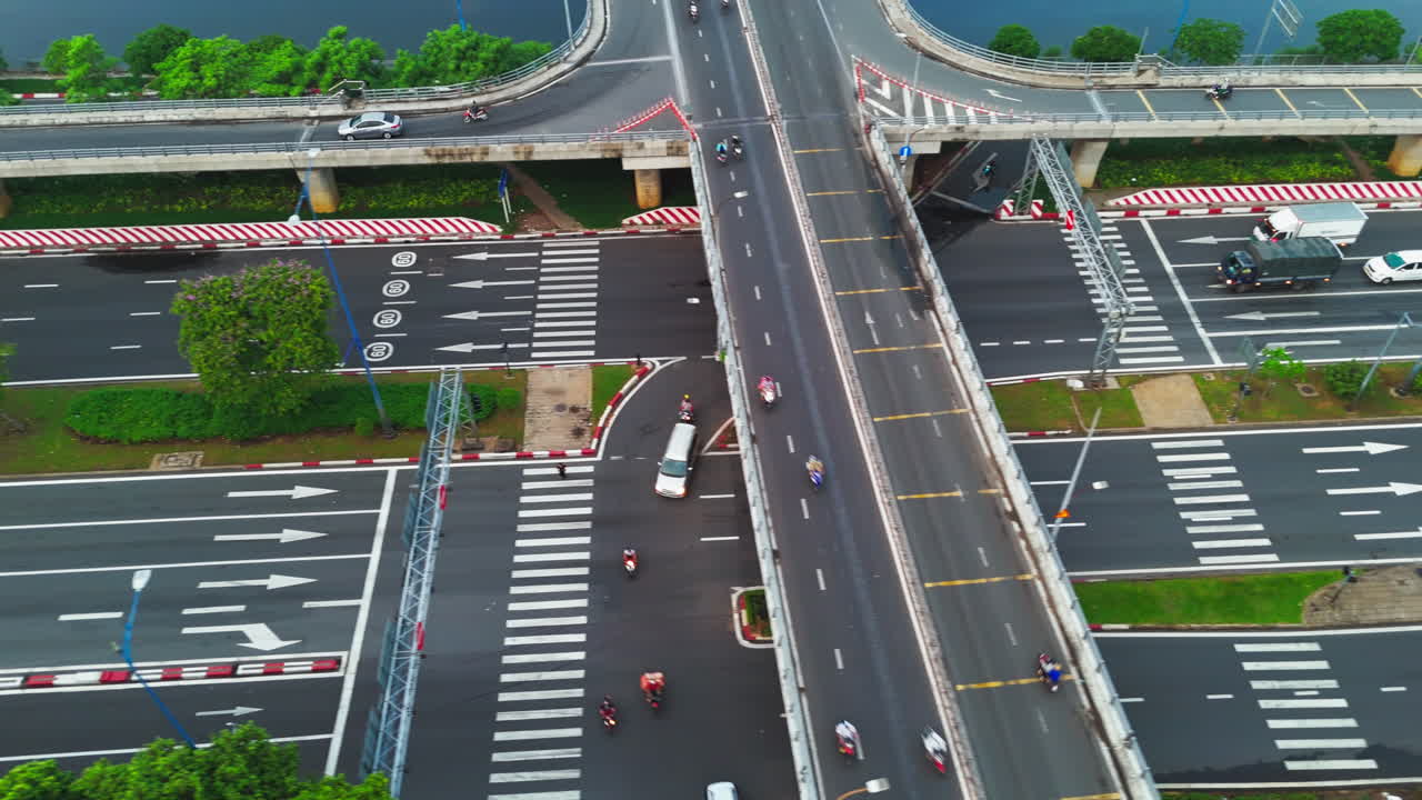 The highway is flanked by lush green trees, providing a refreshing contrast to the concrete jungle. A meandering river cuts through the city, adding to the scenic beauty.
