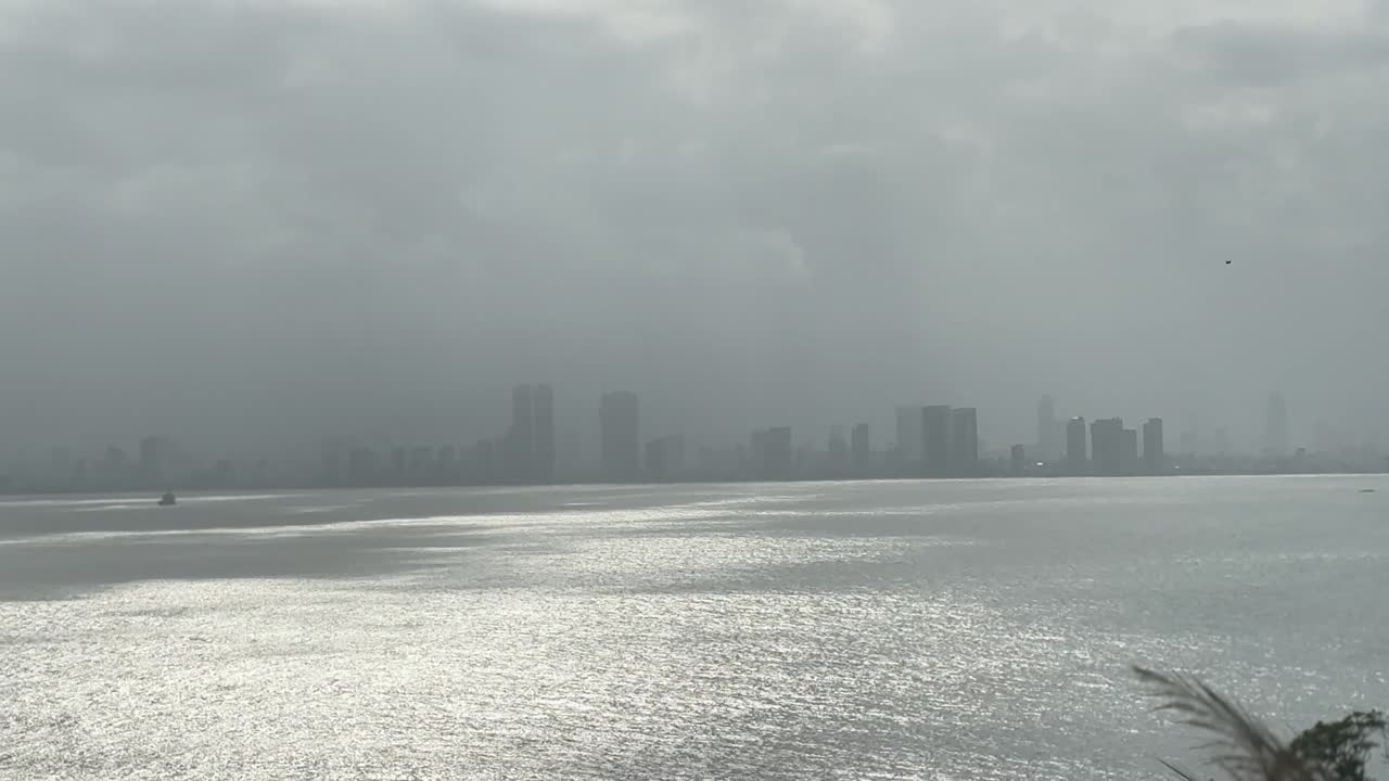 Drone shot capturing Da Nang's skyline with misty atmosphere. Overcast sky reflects on shimmering water. Modern architecture is visible, offering a serene urban landscape