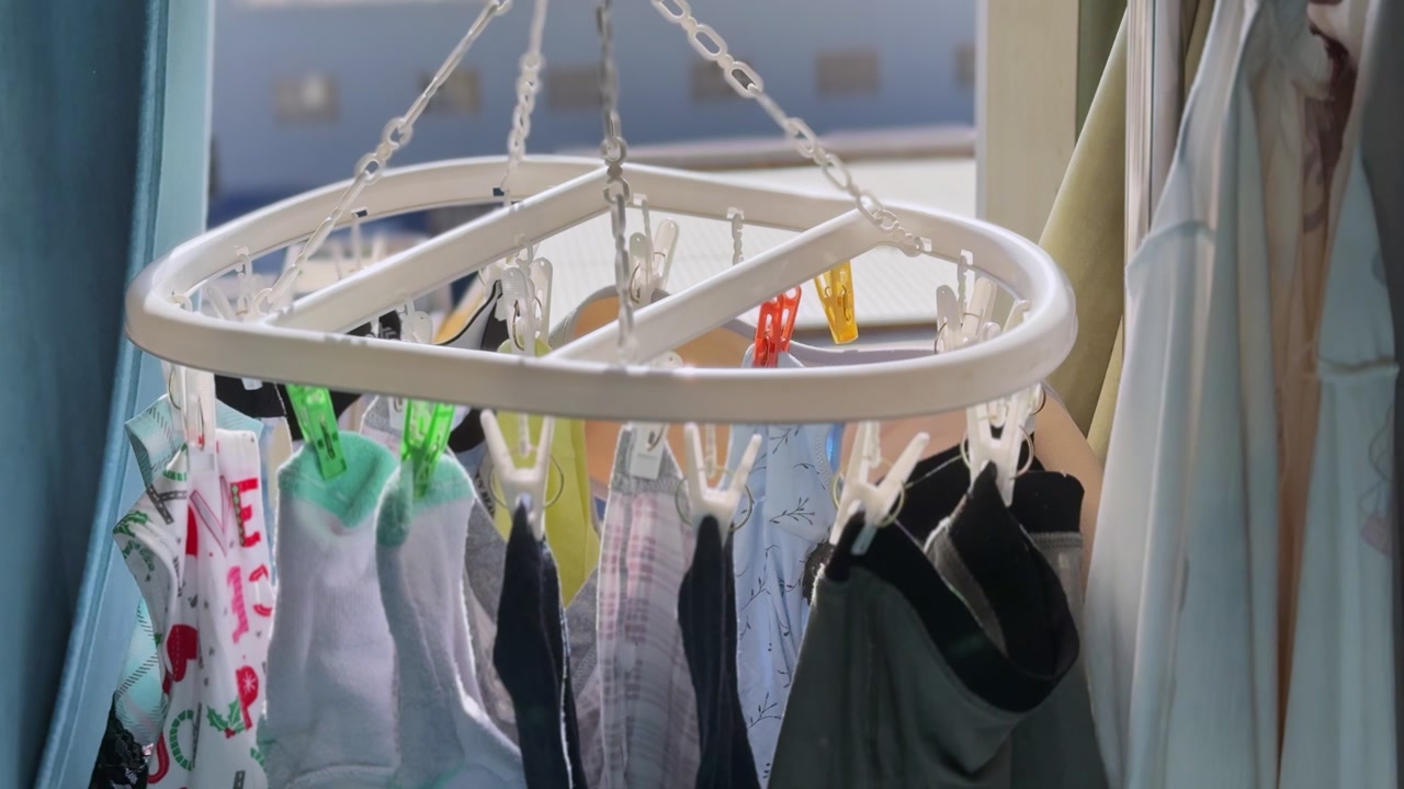 Close-up of socks and garments clipped to a circular indoor drying rack beside a sunlit window, showing everyday home laundry, natural light, and household fabric care.