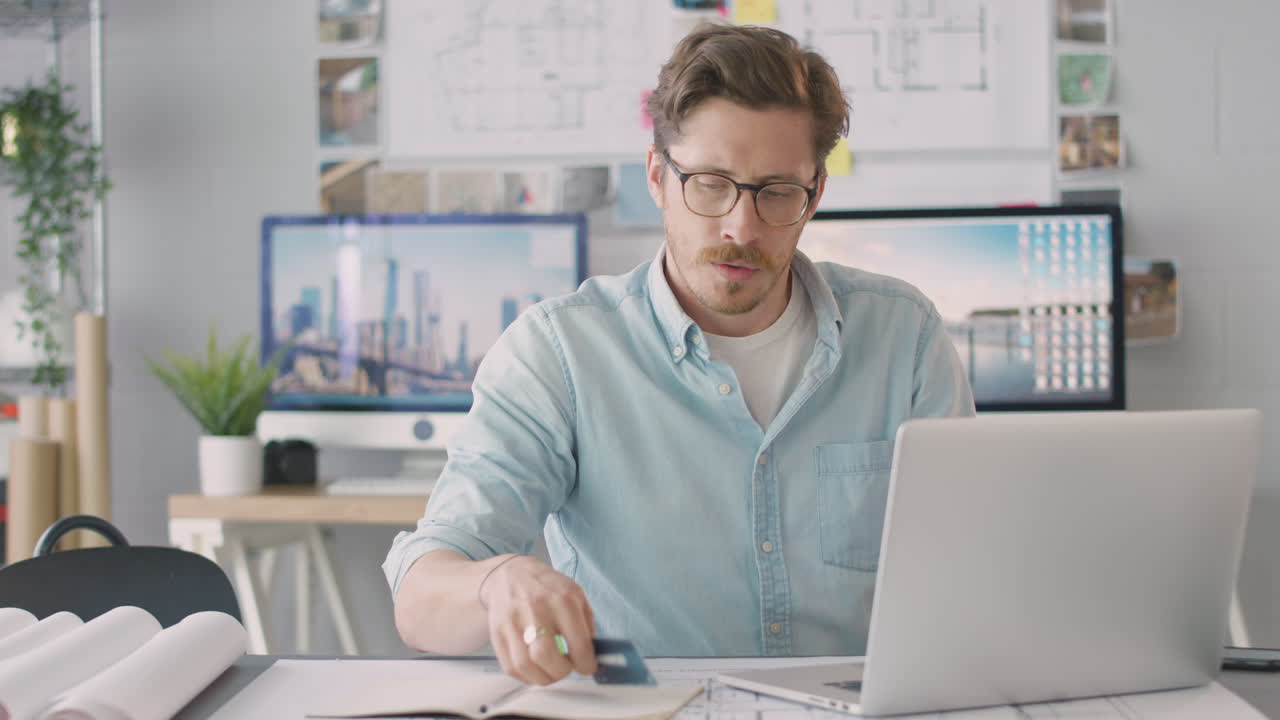 arquitecto masculino en la oficina trabajando en el escritorio haciendo compras en línea usando tarjeta de crédito en la computadora portátil
