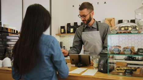 Rückansicht-Einer-Jungen-Kaukasischen-Frau,-Die-Mit-Kreditkarte-Für-Einen-Kaffee-Bezahlt,-Während-Der-Männliche-Barist-Ihr-Einen-Kaffee-Serviert