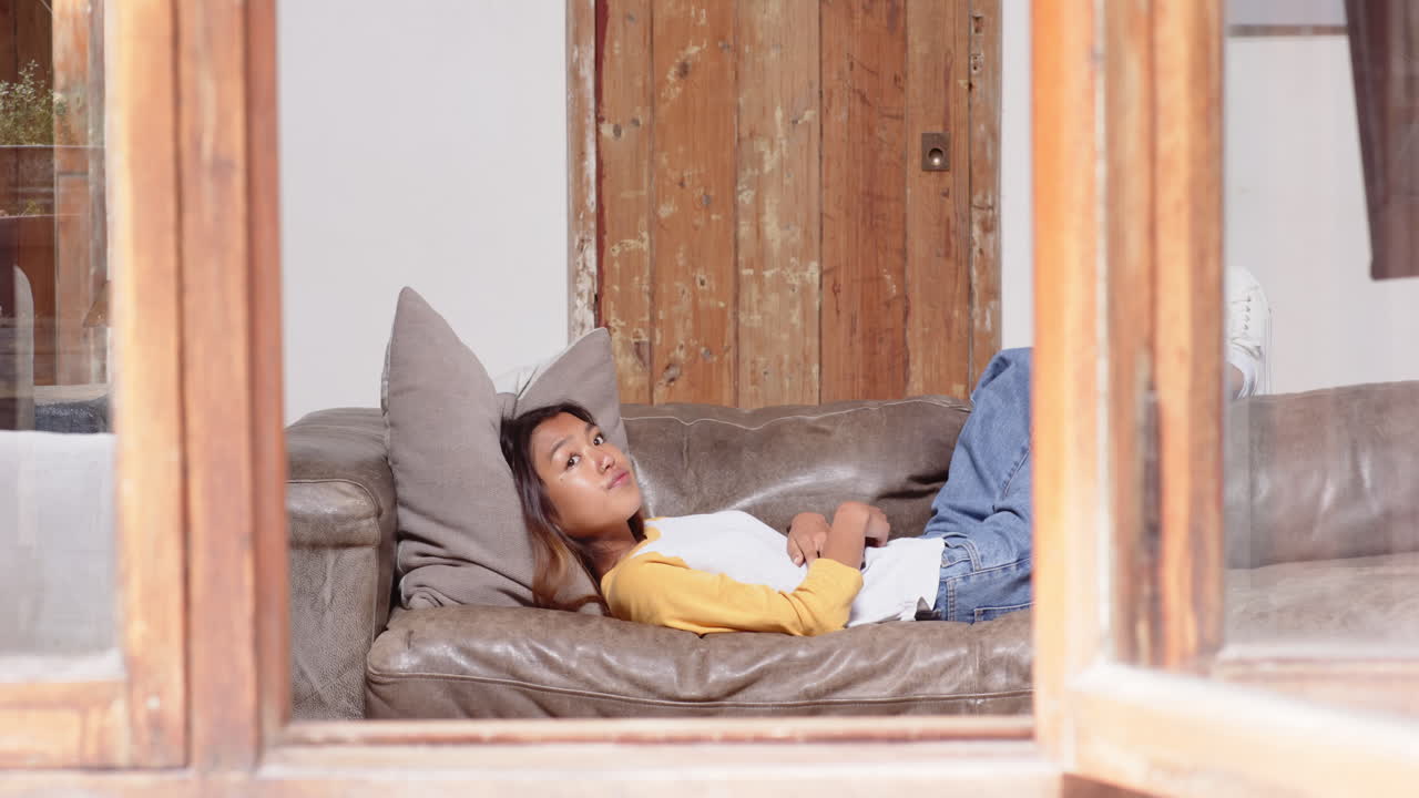 Asian young woman relaxing on sofa at home, enjoying peaceful afternoon