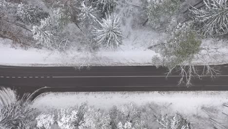 Drone-aerial-view-of-snowy-forest-and-countryside-road-in-Kaunas-county,-Lithuania