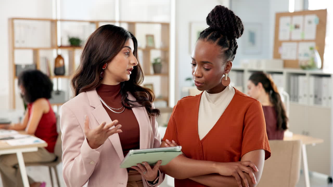 Two Diverse Businesswomen Discussing Project on Digital Tablet in Office