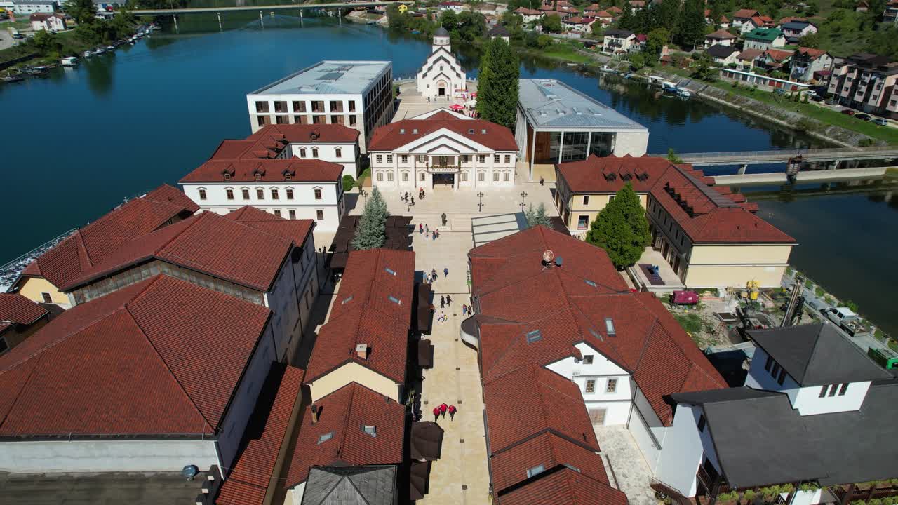 Aerial view of Andricgrad in Visegrad, Bosnia and Herzegovina, featuring stone buildings, red rooftops, river, and historic architecture with surrounding residential neighborhoods and scenic landscape