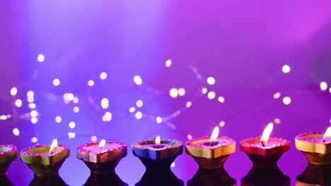 Close-up-of-lights-and-burning-candles-celebrating-diwali-on-purple-background,-with-copy-space