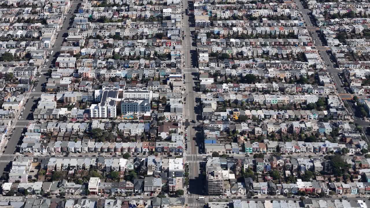 Close-up aerial view of colorful houses in a dense San Francisco neighborhood. Streets form a grid with visible urban planning and local architecture.
