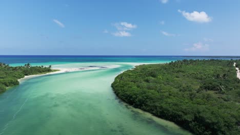 Drone-dolly-above-boardwalk-over-sandy-river-estuary-and-channel-leading-to-blue-ocean-water,-Tulum-Mexico