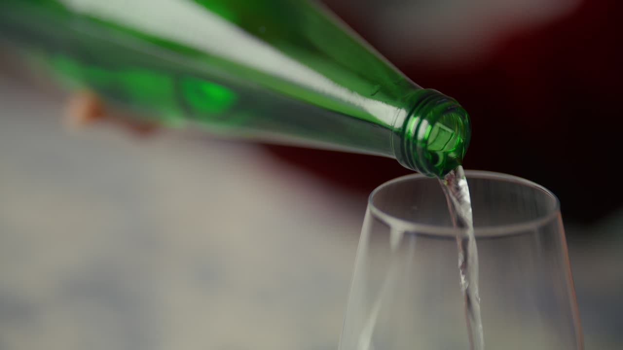 Mano che versa acqua da una bottiglia verde in un bicchiere da vino.