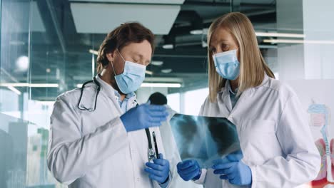 caucasian male and female doctors in medical masks speaking and discussing xray scan in hospital office