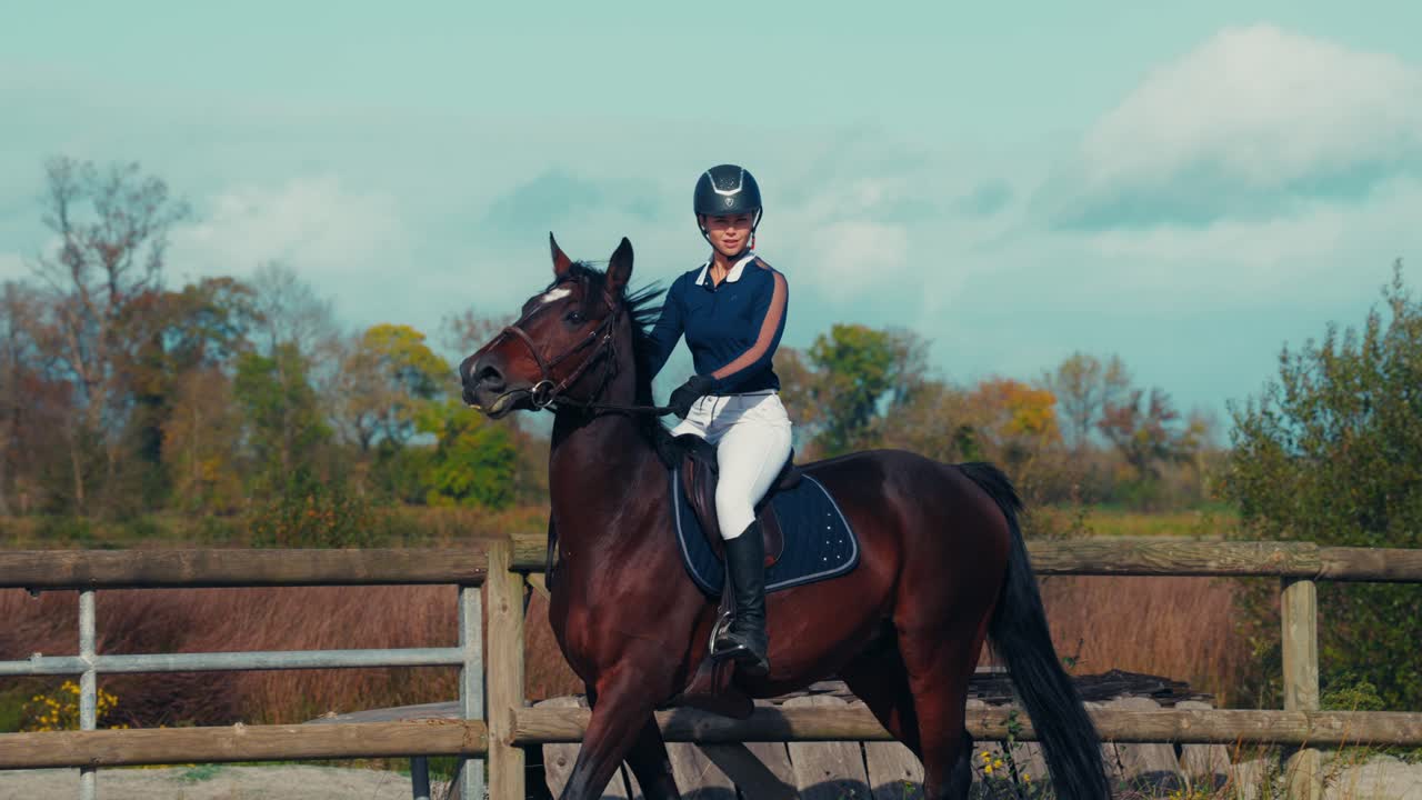 Giovane cavaliere che cavalca un cavallo marrone durante l'allenamento in un'arena esterna. Ambientazione tranquilla di campagna che evidenzia l'equitazione, lo sport equestre e il controllo del cavaliere.