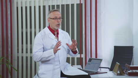 thoughtful mature doctor with laptop on desk in clinic. medic thinks about future cure of a patient.