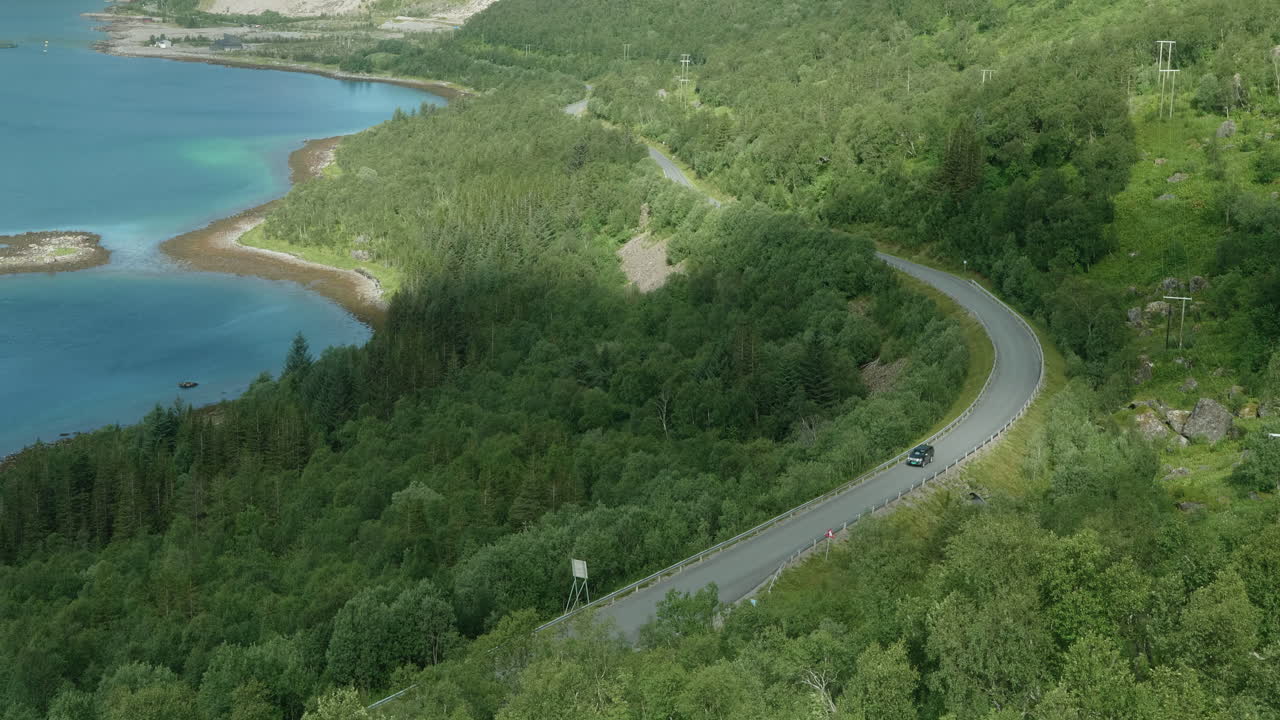 un coche solitario conduciendo en una hermosa carretera en un paisaje de fiordo en el norte de noruega, isla de senja, poco tráfico en un día soleado de verano
