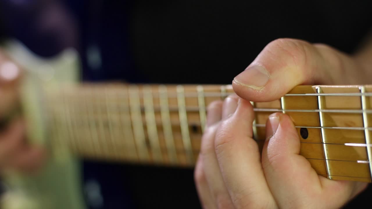 Slow motion close up of an electric stratocasters guitars neck and strings and guitarists hands while playing notes with a pick. Smooth slow motion with stage light scenery. Shot in 4K at 120fps