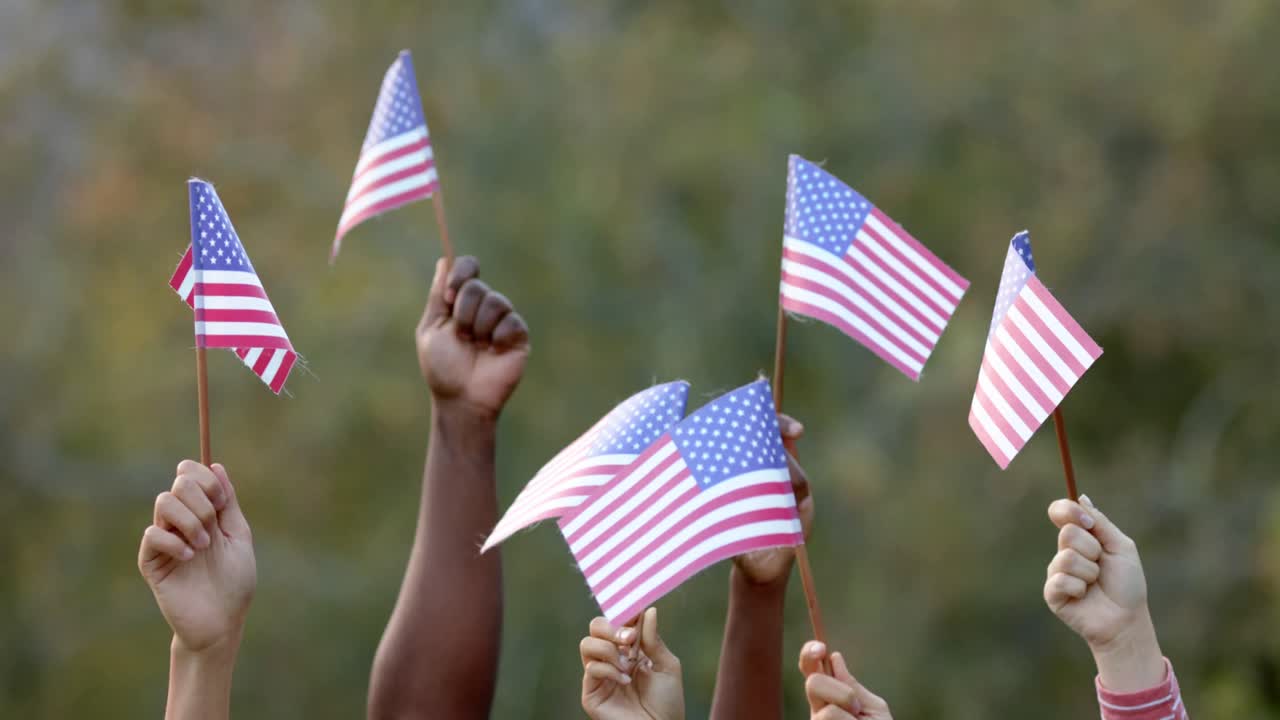 Close up of hands of diverse group of friends holding flags of usa in garden, slow motion