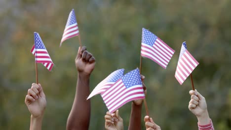 close up of hands of diverse group of friends holding flags of usa in garden, slow motion