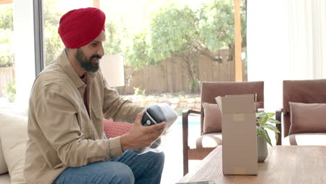 unboxing new electronic device, man in turban sitting on couch smiling