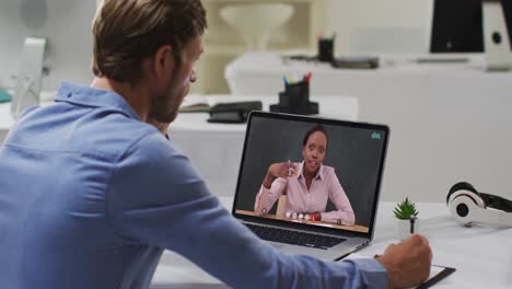 Caucasian-male-student-using-laptop-on-video-call-with-female-teacher,-making-notes