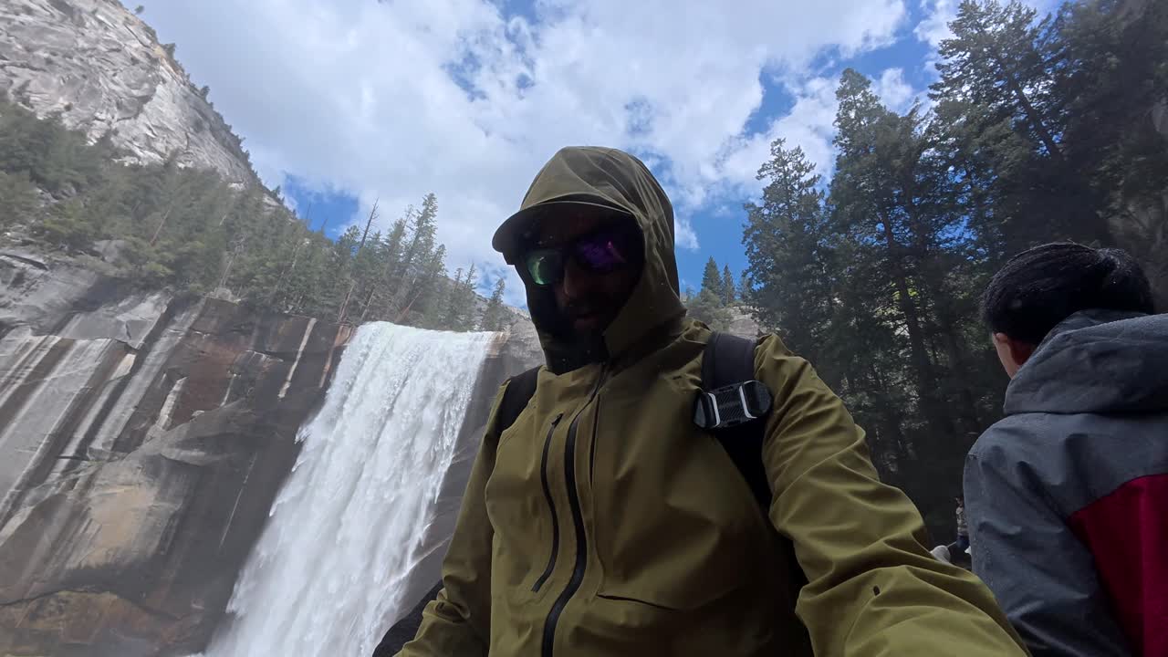 Mand i hættejakke står ved majestætisk vandfald i Yosemite